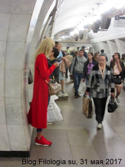 Девушка в красном в красных кроссовках на перроне станции метро в Москве.